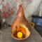 A dried gourd with a carved opening to hold a battery operated candle. Foliage artwork is added to the gourd shell.